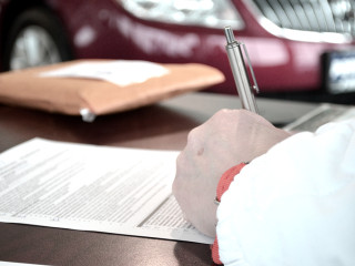a hand signs a form with a car in the background